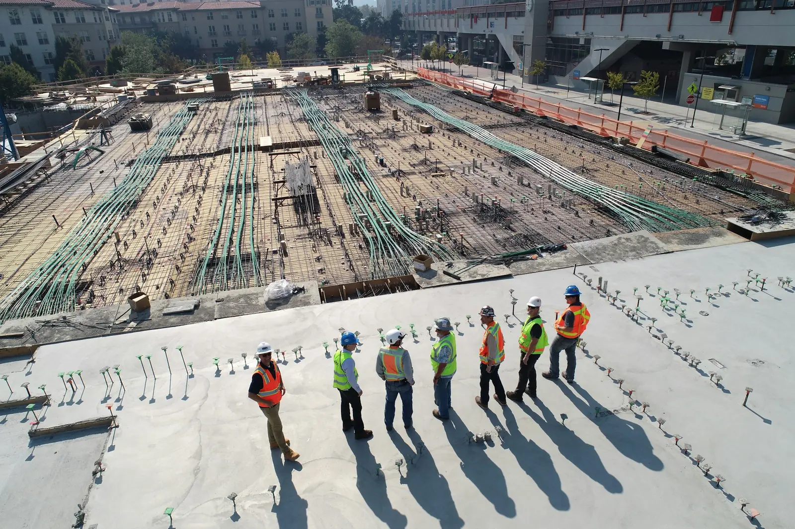 Bauarbeiter mit Warnwesten vor einer großen Baustelle mit Bodenplatte, Symbolbild