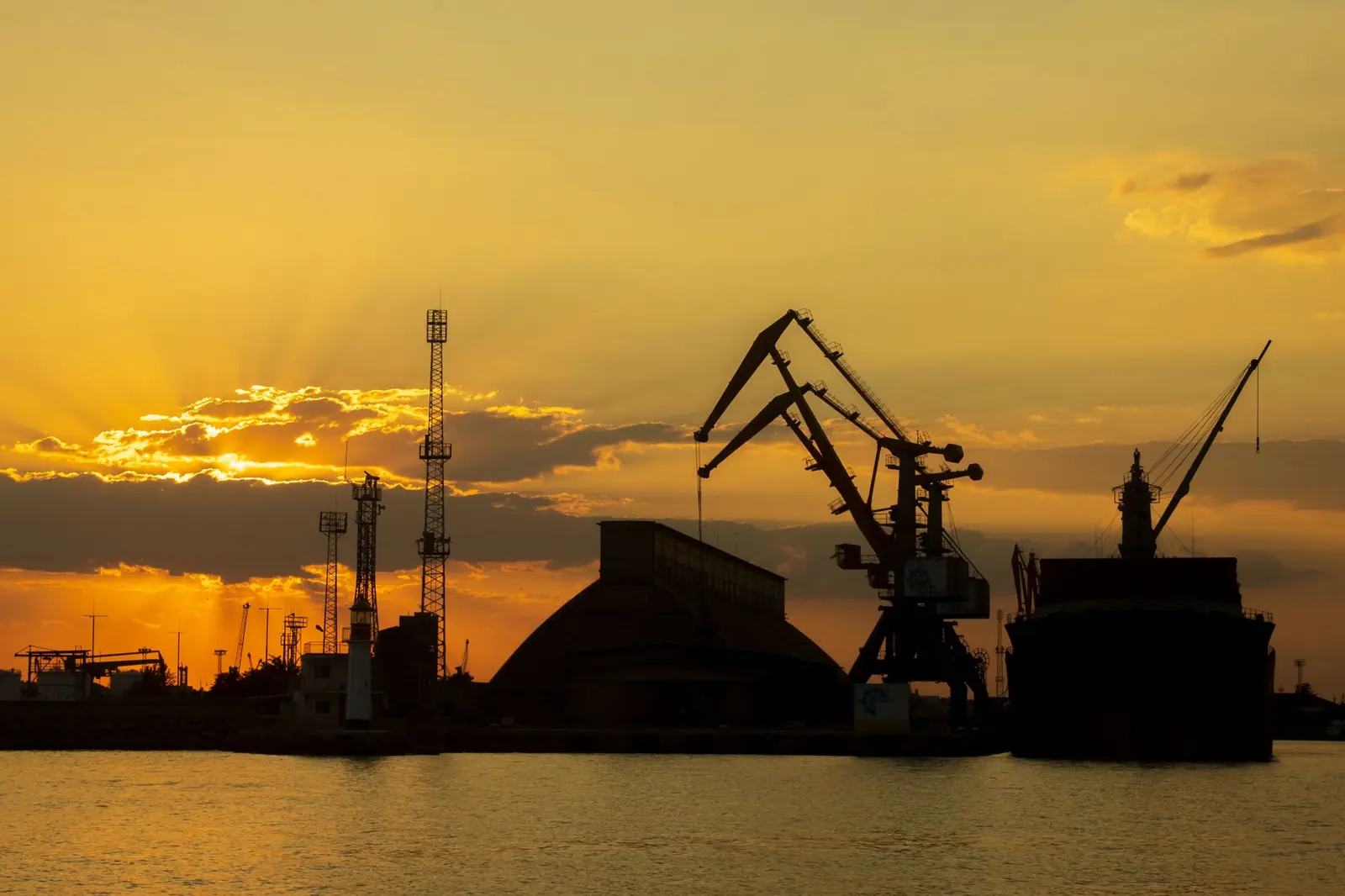 Hafenkräne als Silhouette vor orangefarbenem Abendhimmel, Symbolbild